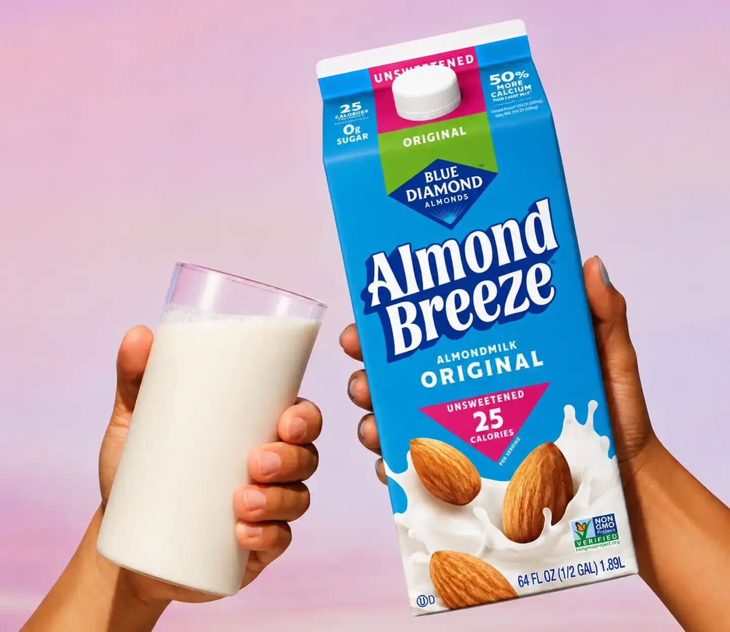 A hand holds a glass of almond milk next to a 64 fl oz carton of Almond Breeze Unsweetened Original almond milk against a pink and purple gradient background.