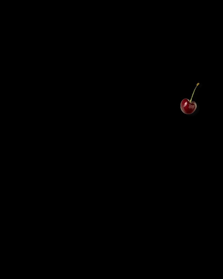 A single red cherry with a green stem is positioned in the lower right corner against a solid black background.