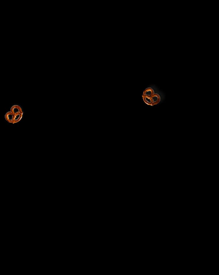 Two small pretzels are placed on a black background, one in the lower left corner and the other in the lower right corner, with ample empty space between them.