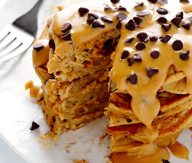Stack of pancakes topped with peanut butter and chocolate chips, with a slice cut out, served on a white plate with a fork nearby.