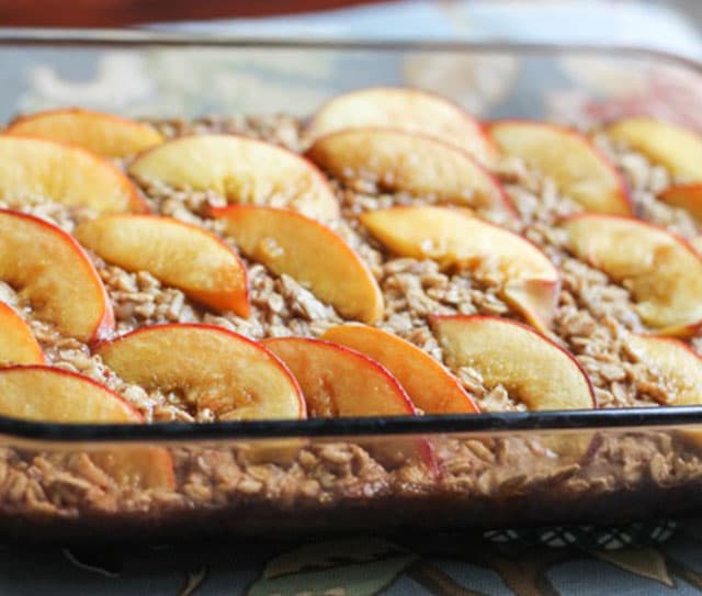 Glass baking dish filled with baked oatmeal, topped with neatly arranged slices of fresh peaches.