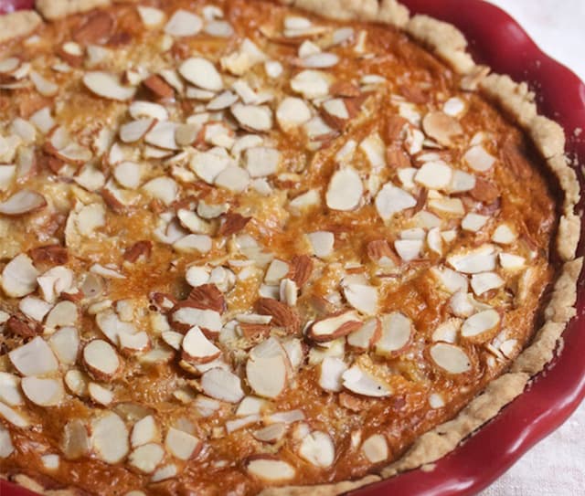 A baked pie in a red dish topped with sliced almonds, featuring a golden-brown crust and filling.