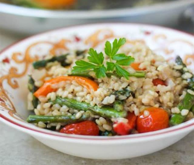 A bowl of rice mixed with asparagus, cherry tomatoes, and red bell peppers, garnished with a sprig of parsley.