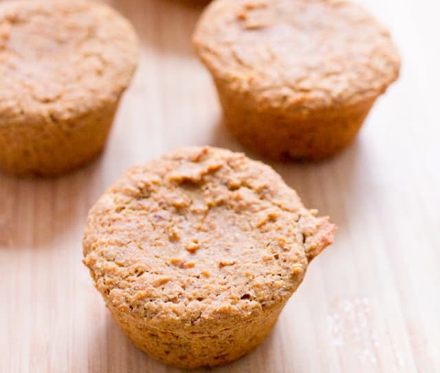 Three baked muffins with a golden-brown crust are arranged on a wooden surface, with one muffin in clear focus at the front.