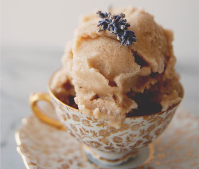 A scoop of ice cream topped with a sprig of lavender, served in a gold-patterned teacup on a matching saucer.
