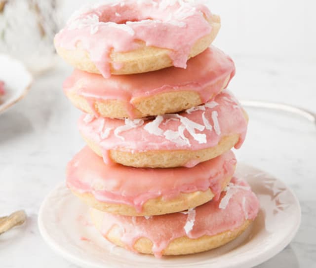 A stack of four donuts with pink icing and coconut flakes sits on a white plate.