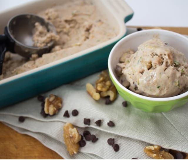 A bowl of ice cream with chocolate chips and walnuts sits next to a dish of more ice cream, scattered walnuts, and chocolate chips on a napkin.