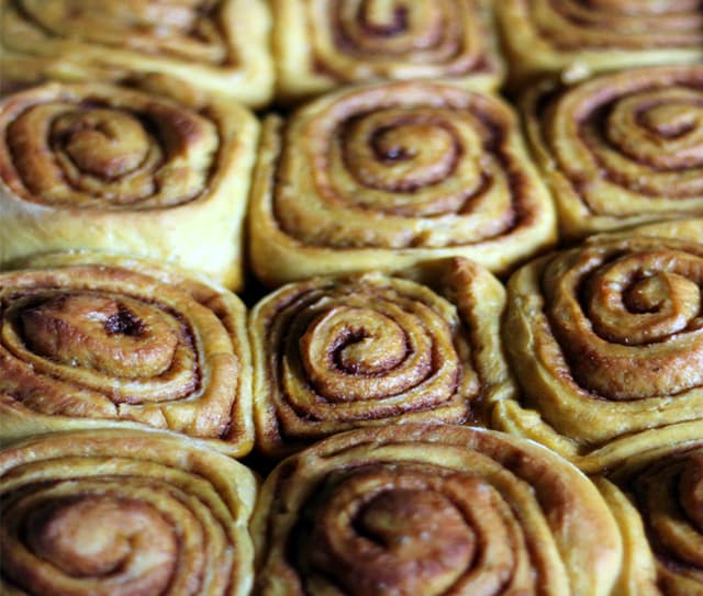 Close-up of nine cinnamon rolls baked closely together, showing golden-brown swirls and a slightly glossy surface.