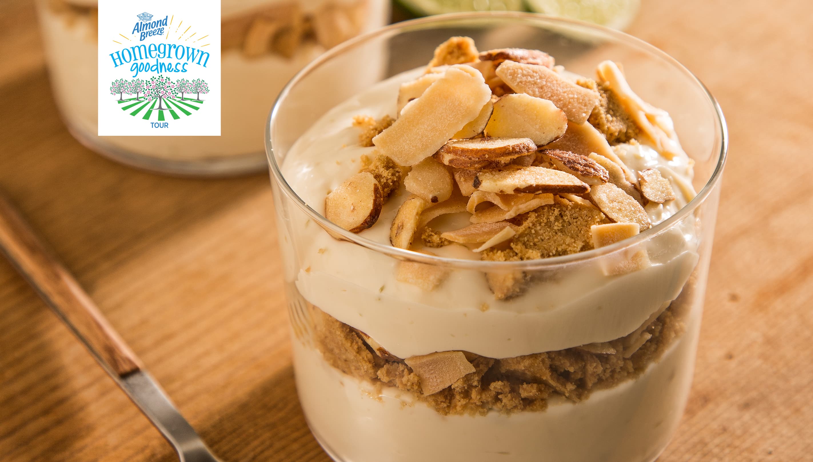 A glass cup filled with creamy dessert topped with toasted coconut flakes and cookie crumbs sits on a wooden surface.