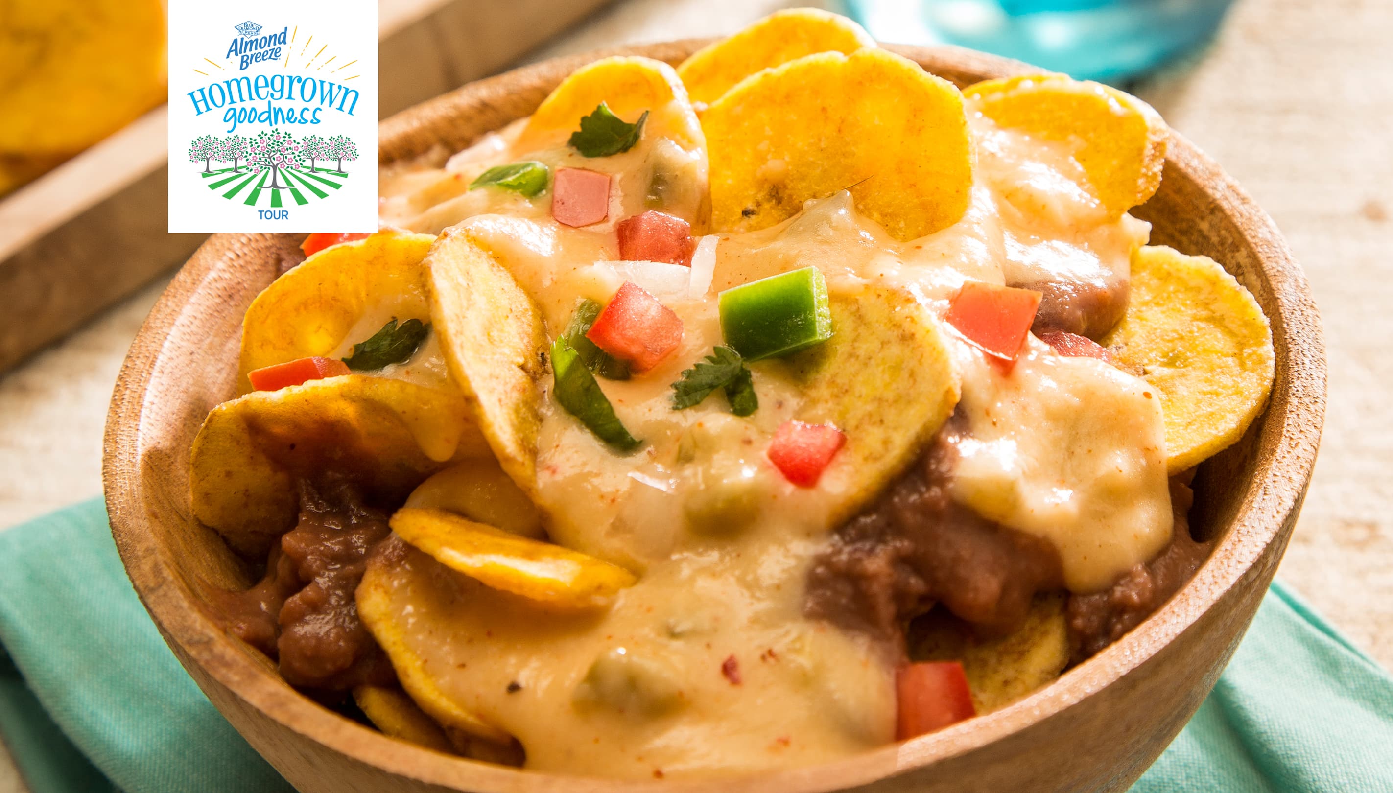 A wooden bowl filled with nachos topped with melted cheese, beans, diced tomatoes, green peppers, and cilantro.