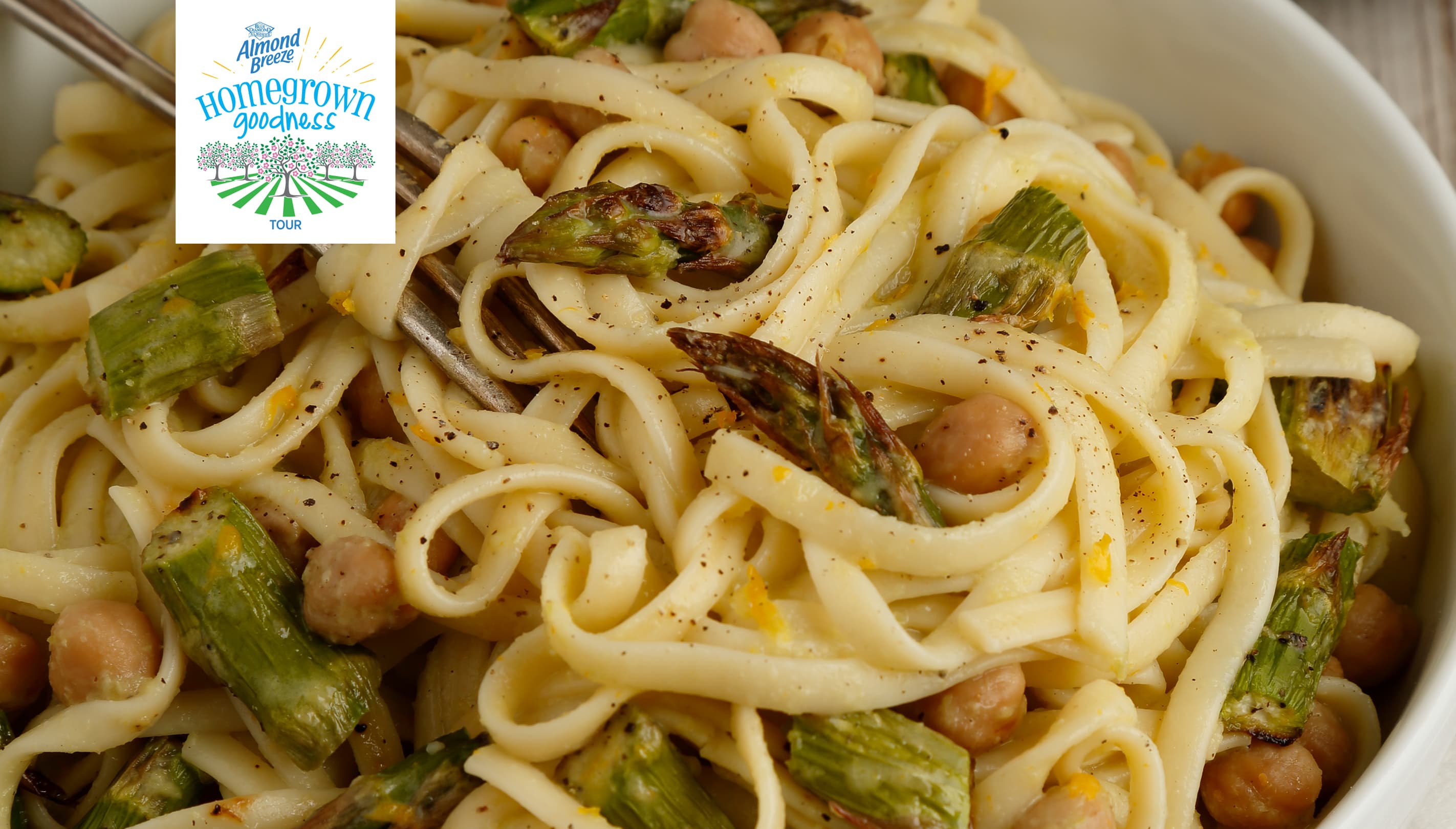 A bowl of linguine pasta with roasted asparagus and chickpeas, seasoned with pepper. A logo in the top left corner reads Hometown Goodness Tour..