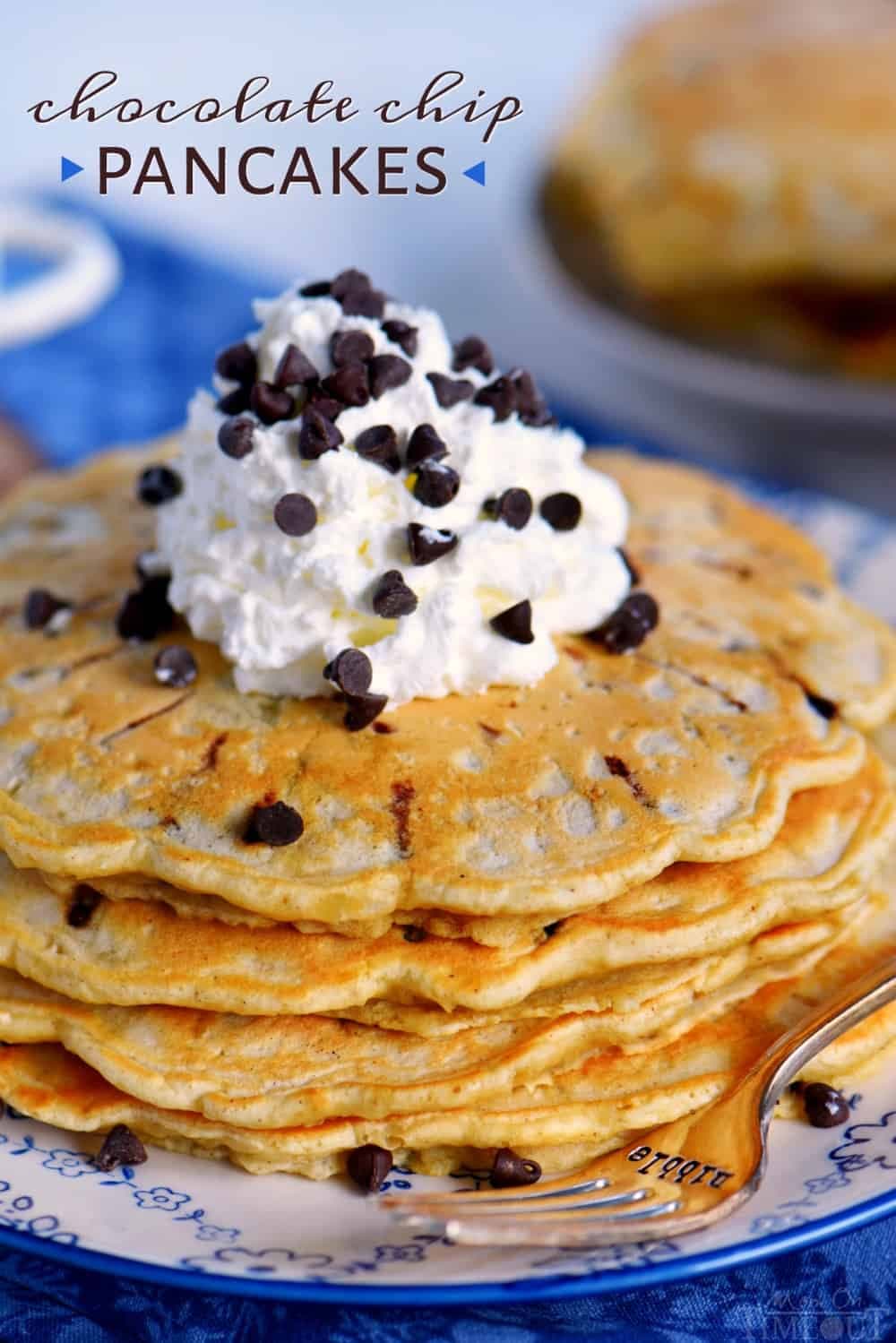A stack of chocolate chip pancakes topped with whipped cream and more chocolate chips on a plate with a fork.