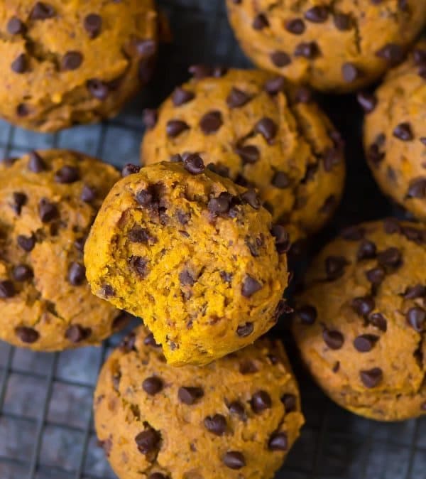 A batch of pumpkin chocolate chip cookies on a cooling rack, with one cookie showing a bite taken out of it.