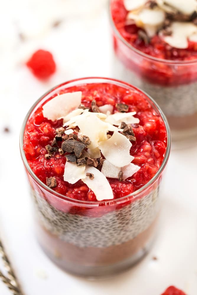 A glass cup filled with chia pudding, topped with raspberry compote, cacao nibs, and coconut flakes, seen from above.