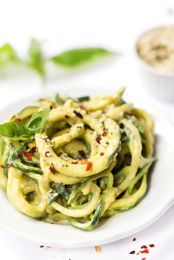 Zucchini noodles topped with creamy sauce, garnished with red pepper flakes and herbs, served on a white plate.
