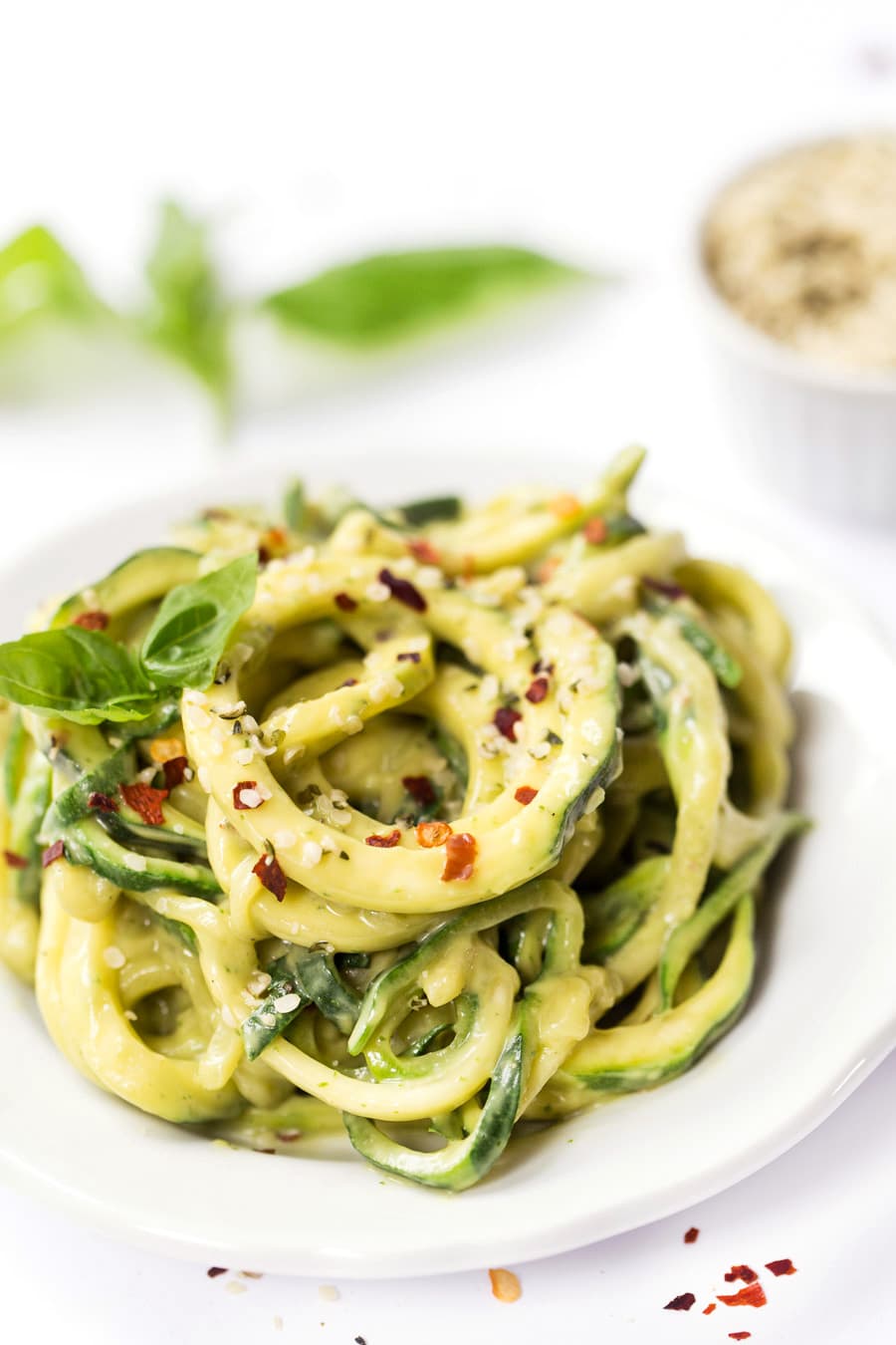 Zucchini noodles topped with creamy sauce, garnished with red pepper flakes and herbs, served on a white plate.