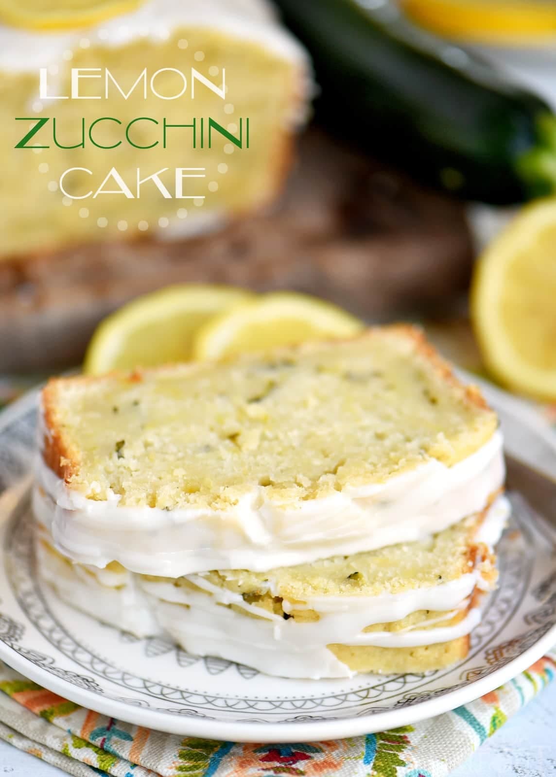 Two slices of lemon zucchini cake with white icing on a decorative plate, with lemon and zucchini in the background.