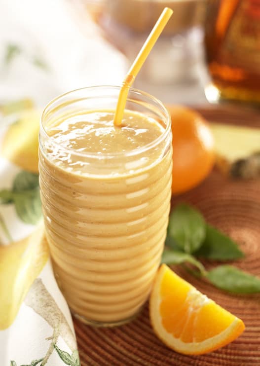 A tall glass filled with a creamy orange smoothie, served with a yellow straw and garnished with a fresh orange wedge on a wooden surface.