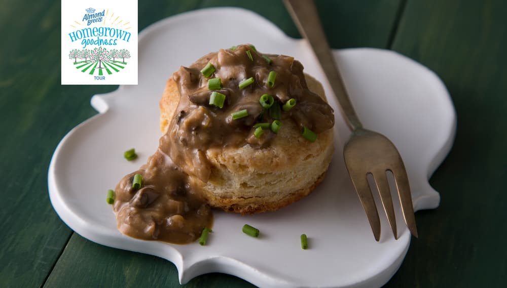 A biscuit topped with brown gravy and chopped chives sits on a white plate with a fork. The Hometown Goodness logo appears in the top left corner of the image.