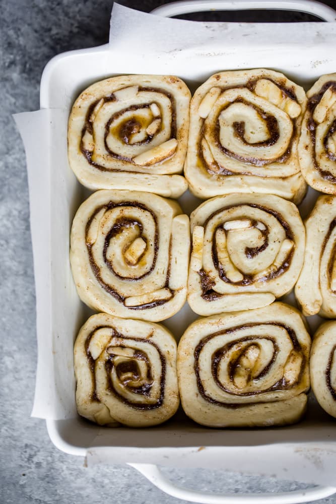 Unbaked cinnamon rolls arranged closely together in a white rectangular baking dish, ready to go into the oven.