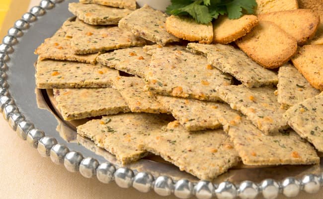 A silver tray with square and round crackers arranged in rows, garnished with fresh herbs.