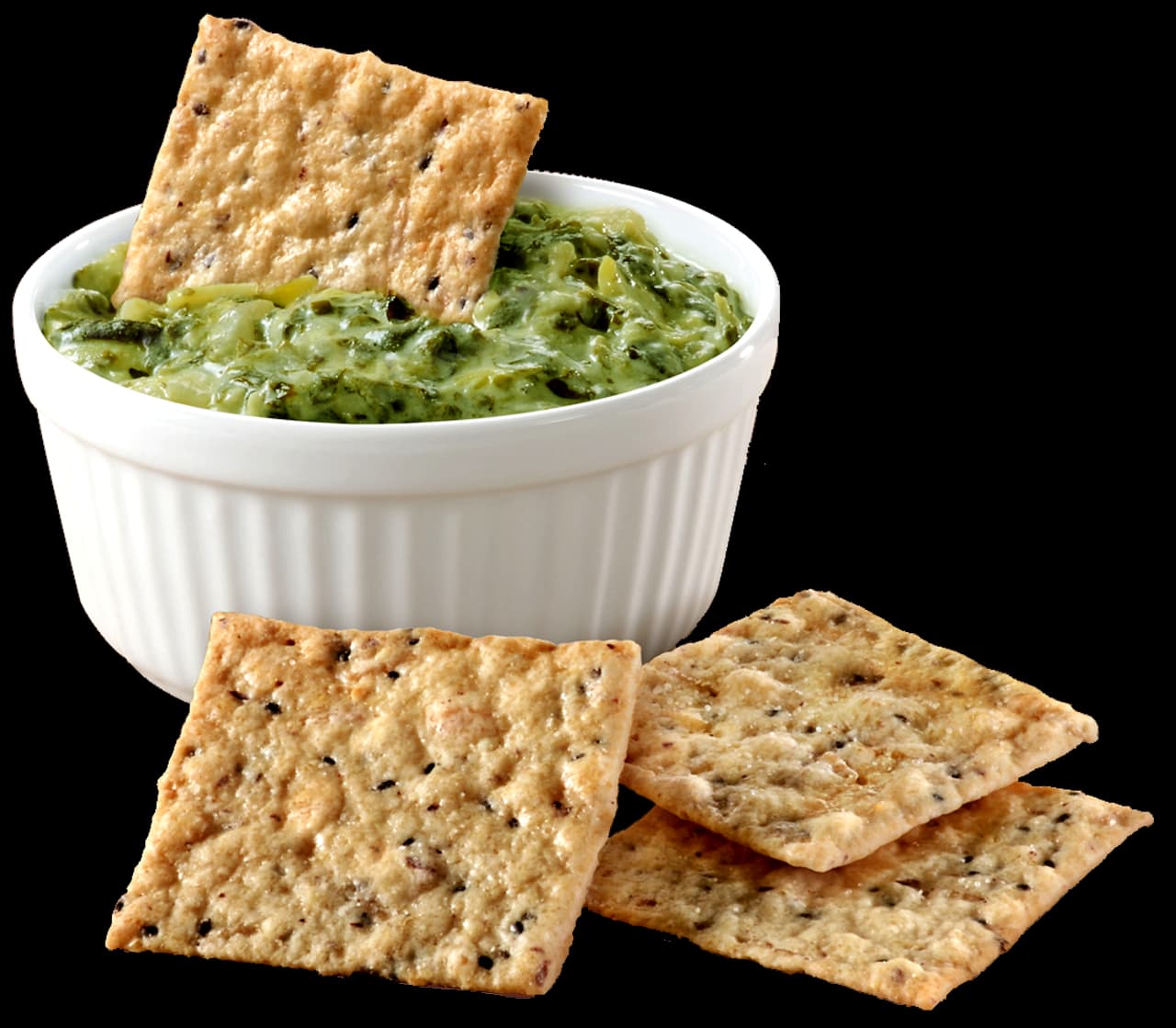 A white ramekin filled with green dip, with a cracker inside, is placed next to three square crackers on a white surface.