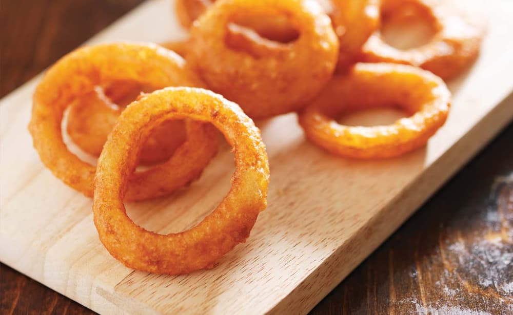 A close-up of several golden-brown fried onion rings arranged on a wooden serving board.