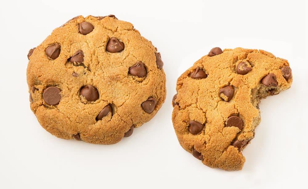 Two chocolate chip cookies on a white background, with one cookie whole and the other missing a bite.