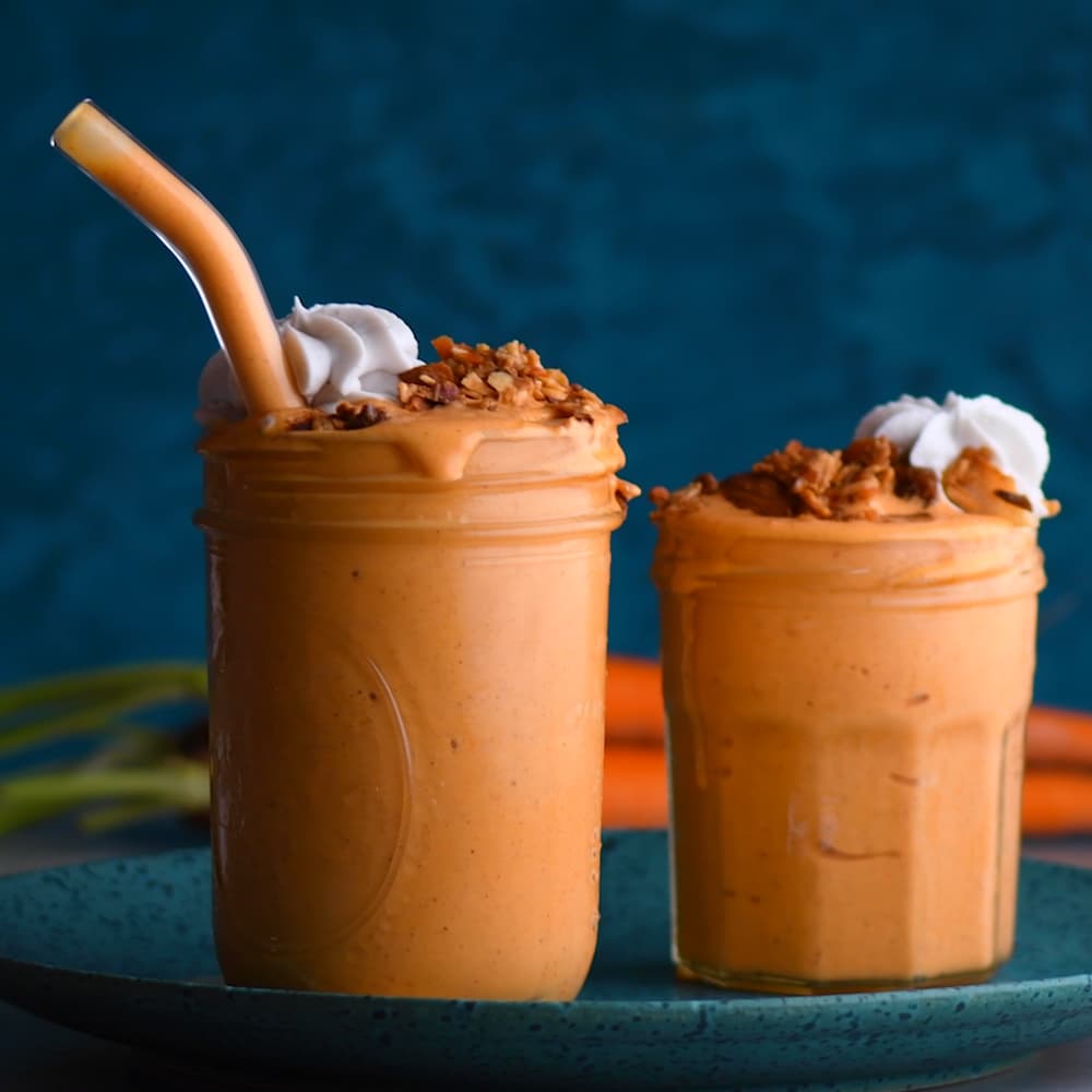 Two glass jars filled with orange smoothie, topped with granola and whipped cream, are placed on a plate against a dark blue background.