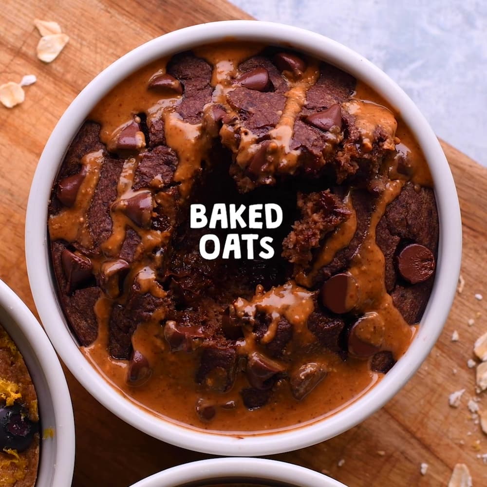 A white ramekin filled with chocolate chip baked oats drizzled with peanut butter sits on a wooden surface. The words BAKED OATS are centered over the oats.