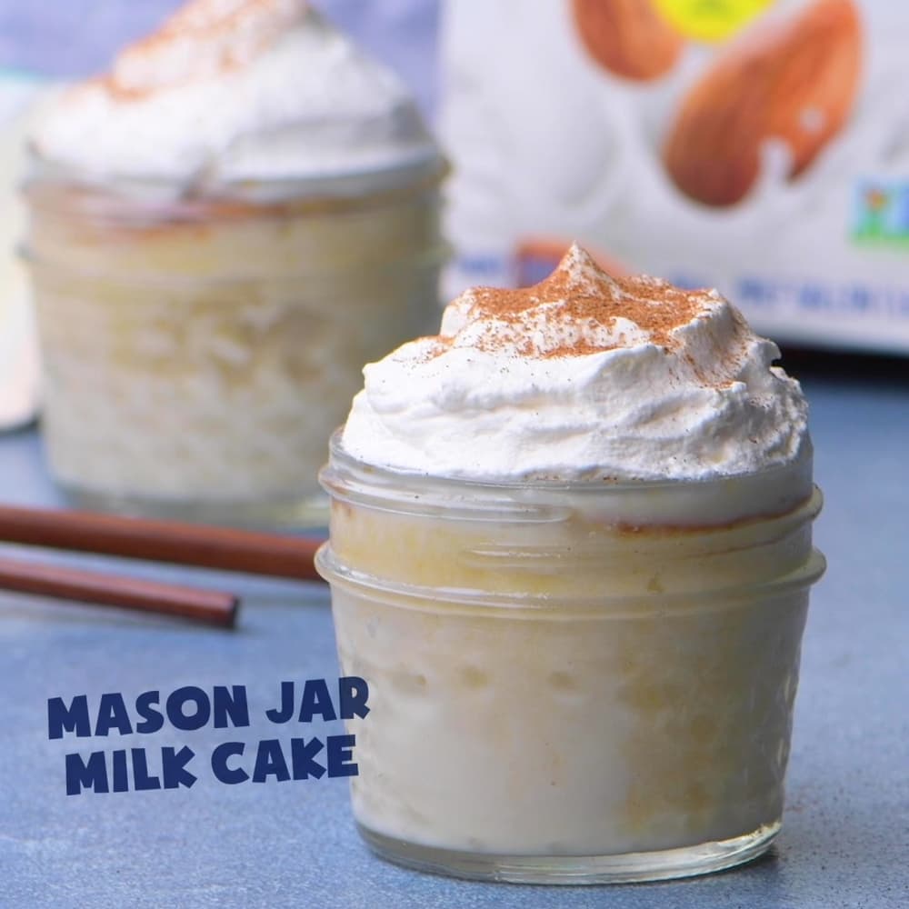 Two small mason jars filled with milk cake, topped with whipped cream and a sprinkle of cinnamon, with Mason Jar Milk Cake text in the foreground.