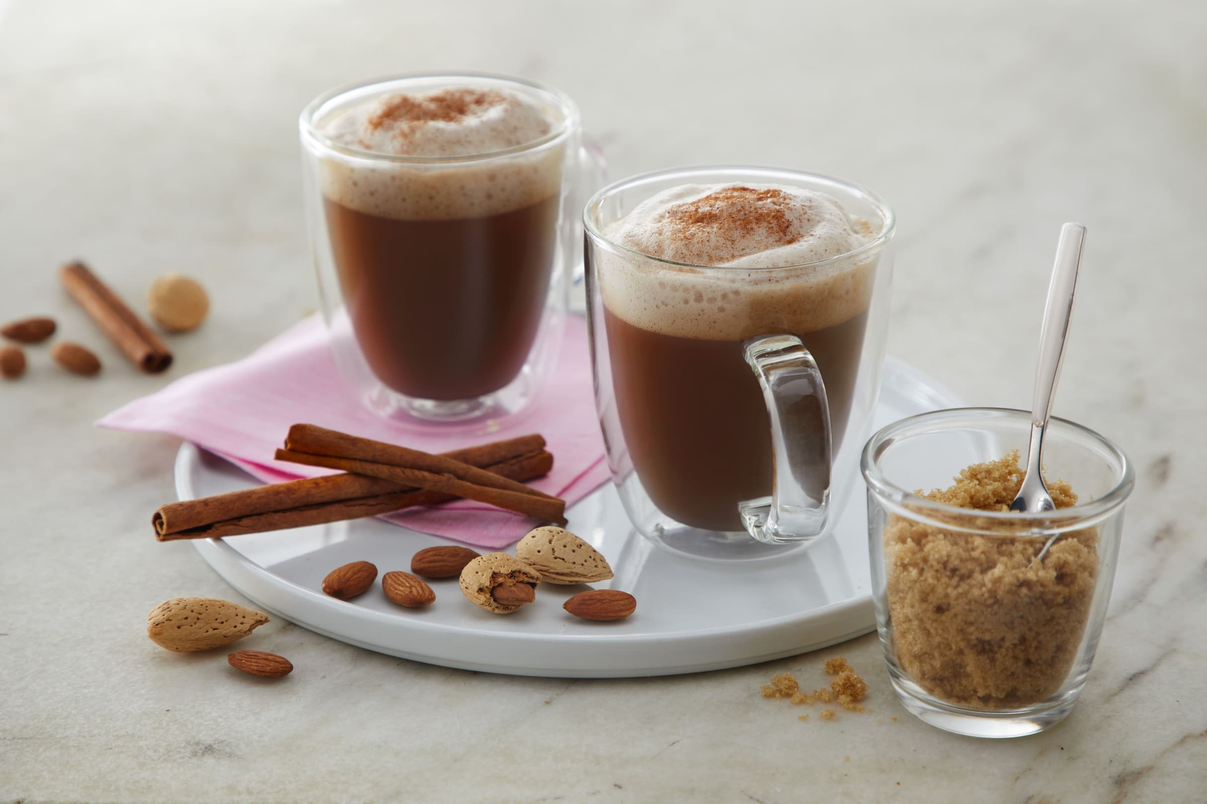 Counter top with two mugs full of cinnamon brown sugar lattes decorated with cinnamon sticks and Blue Diamond Almonds