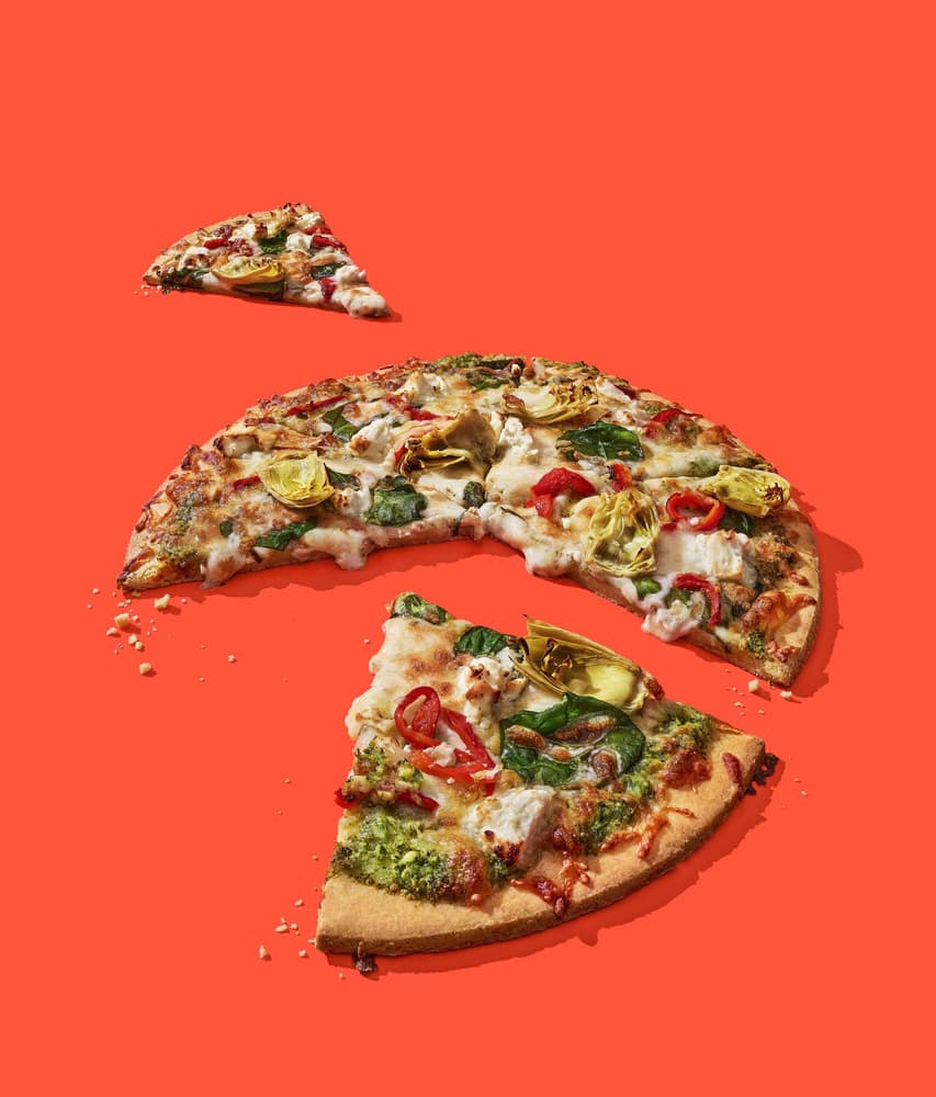 A whole vegetable pizza with two slices removed, one placed nearby and one set further away, arranged on an orange background.