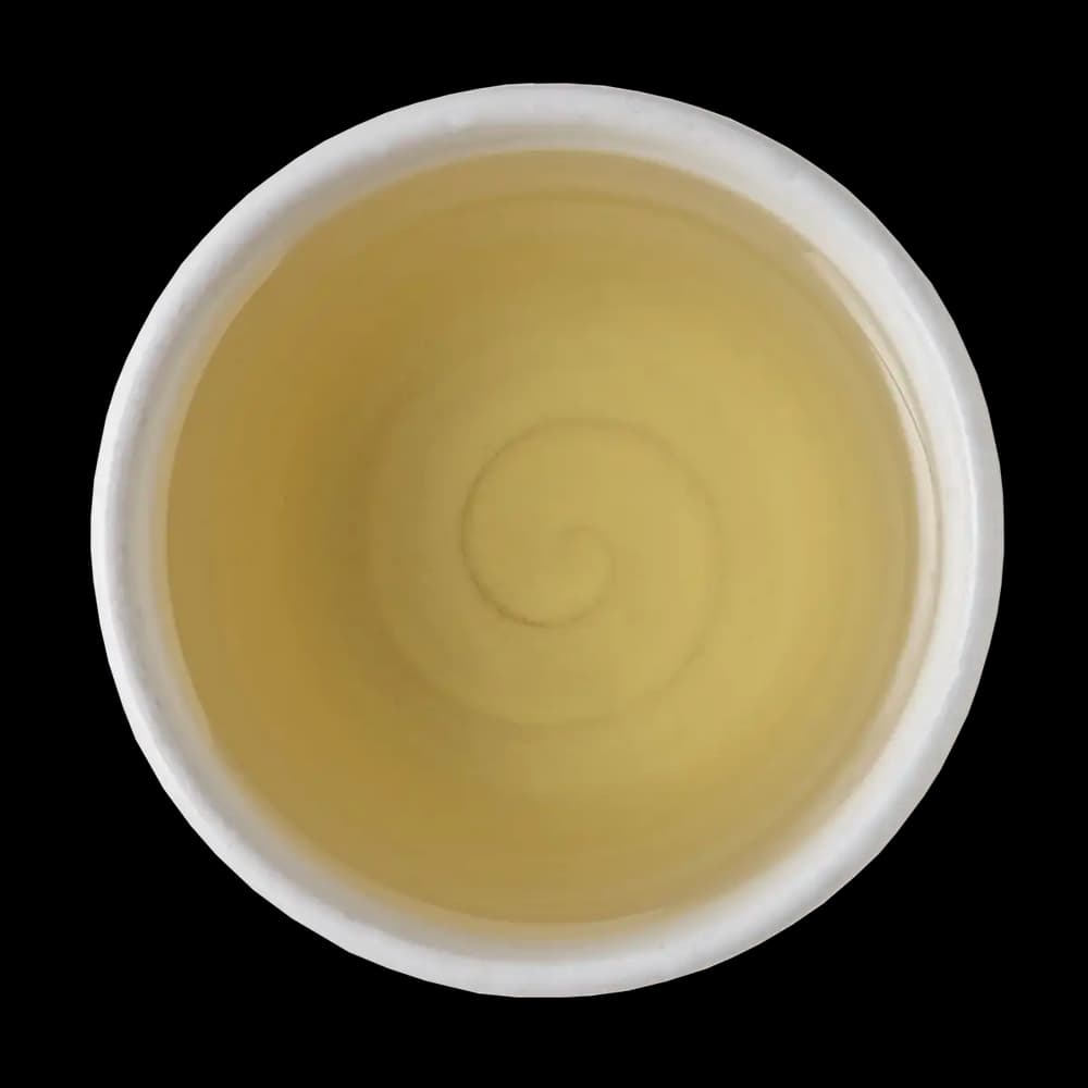 Top view of a white cup filled with light yellow liquid, showing a visible swirl pattern in the center, on a black background.