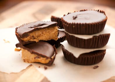 Four chocolate peanut butter cups on parchment paper, with one cup partially bitten to reveal the peanut butter filling.