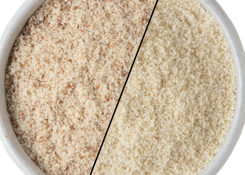 A bowl divided diagonally, showing two types of ground almond flour: finely ground with skins on the left, and blanched, lighter flour without skins on the right.