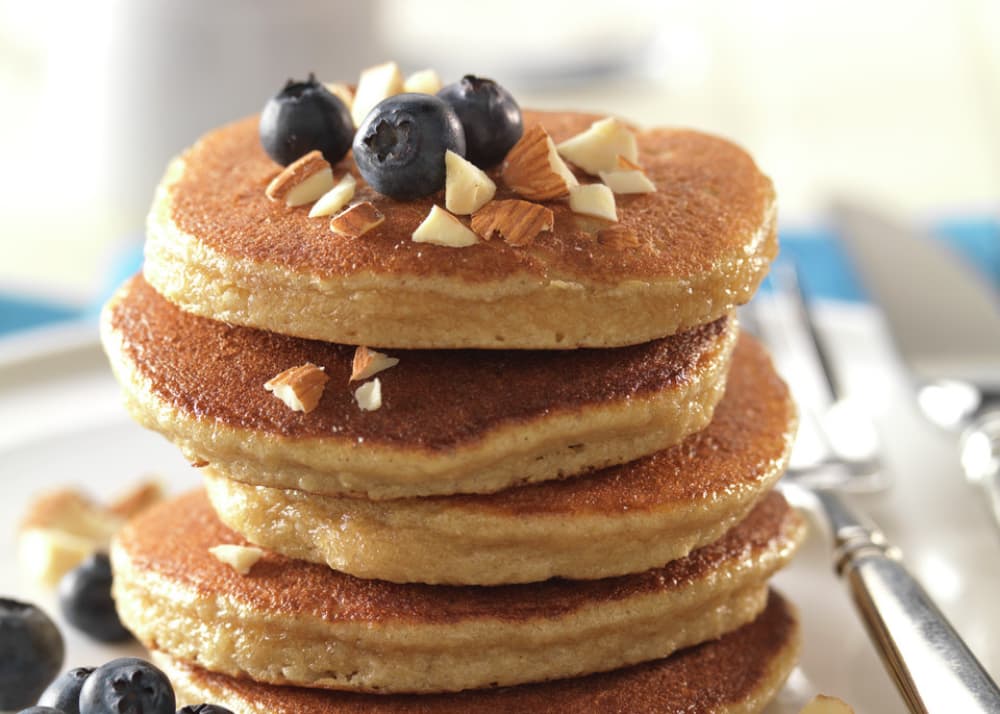 A stack of pancakes topped with blueberries and chopped nuts, with additional blueberries on the plate beside silverware.