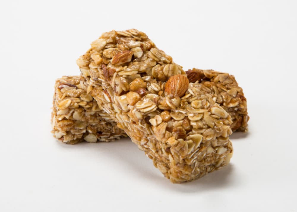 Two granola bars with visible oats, nuts, and seeds are stacked on a plain white background.