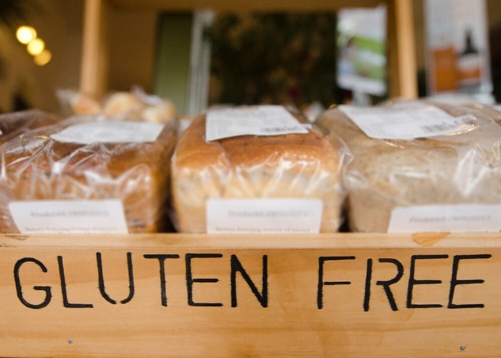 Several loaves of packaged bread are displayed on a wooden shelf labeled GLUTEN FREE in black letters.
