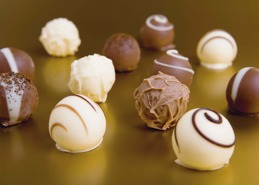 Assorted chocolate truffles in white and milk chocolate are arranged on a smooth, gold surface.