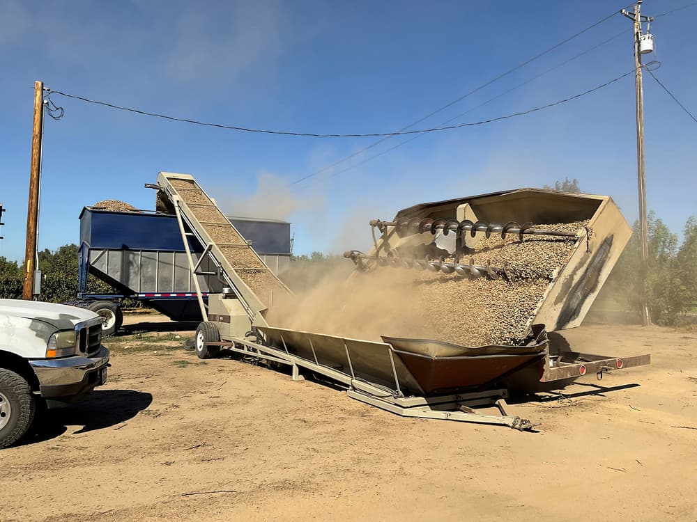A machine processes and sorts gravel on a construction site, with dust rising in the air, and a truck and utility pole visible nearby.