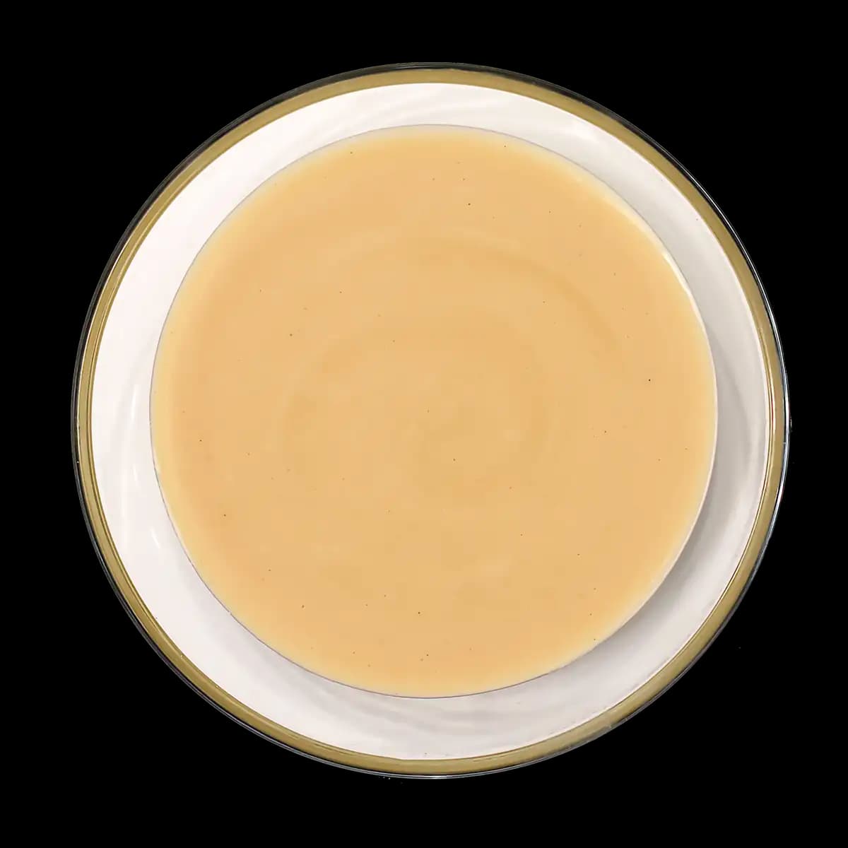 A bowl filled with light beige creamy sauce, viewed from above, set against a black background.