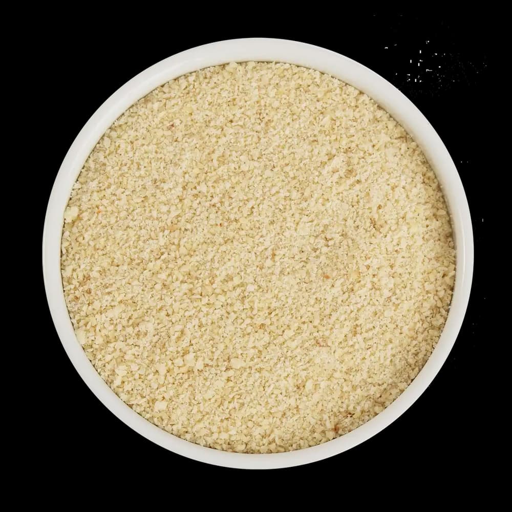 A white bowl filled with light-colored, finely ground breadcrumbs, pictured from above against a black background.