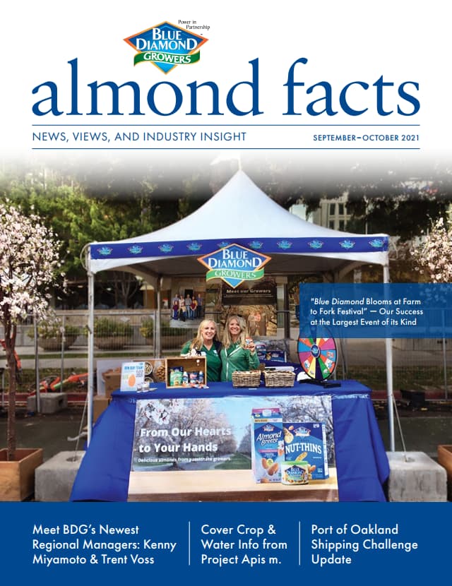 Two people stand at a Blue Diamond Growers booth displaying almond products and informational materials under a tent at an outdoor event.