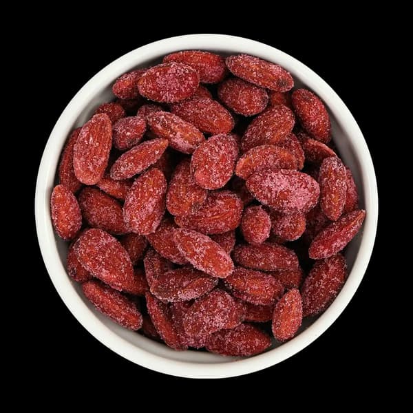 A white bowl filled with red, sugar-coated almonds sits on a solid black background.