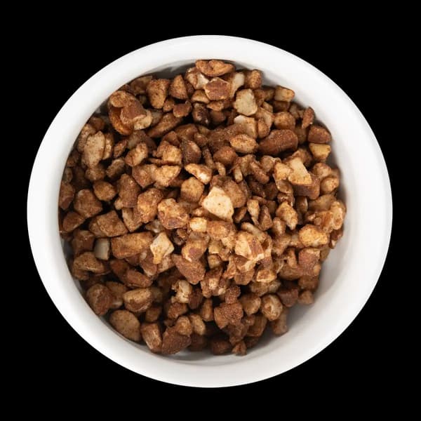 A white bowl filled with chopped nuts coated in a brown seasoning, photographed from above against a black background.