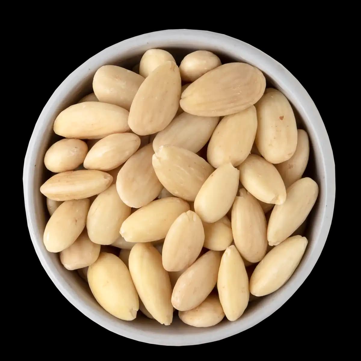 A white bowl filled with blanched, skinless almonds is shown against a black background.
