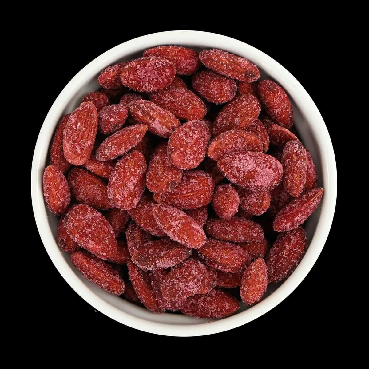 A white bowl filled with red, sugar-coated dried plums, viewed from above, set against a black background.